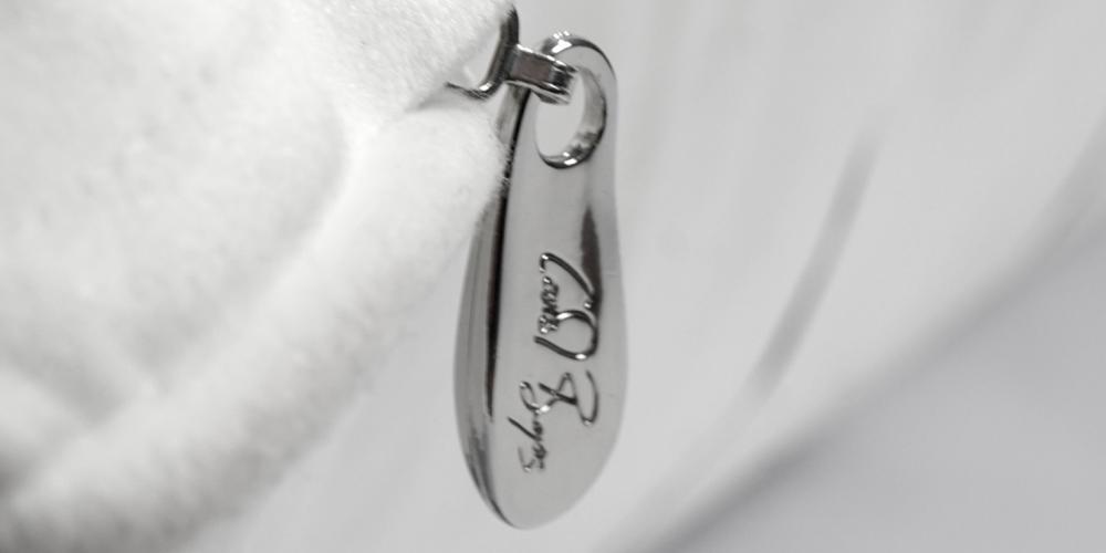 Polished metal keychain with engraved signature hanging from a white background.