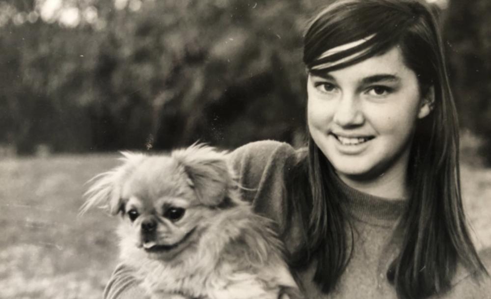 A black-and-white photograph of a young Carrol Boyes smiling while holding a small dog.