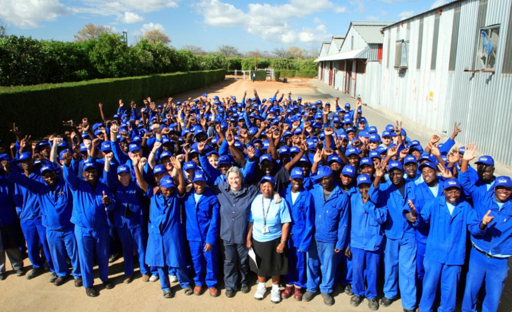 Group of workers in blue uniforms, smiling and raising hands outside