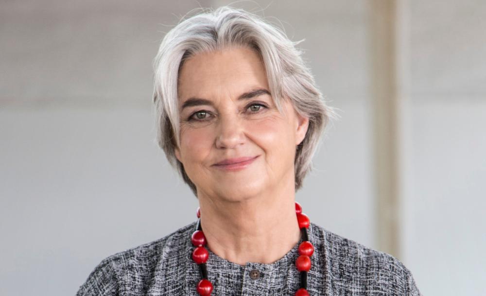 Carrol Boyes smiling, wearing a gray outfit with a red beaded necklace