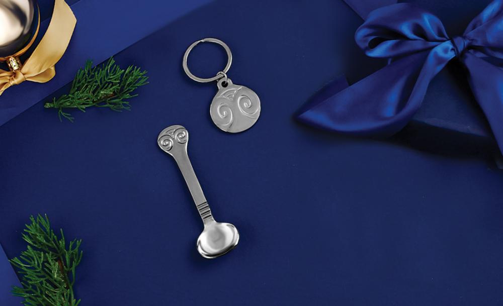 Decorative spoon and keyring with swirling patterns on a deep blue background, surrounded by festive greenery.